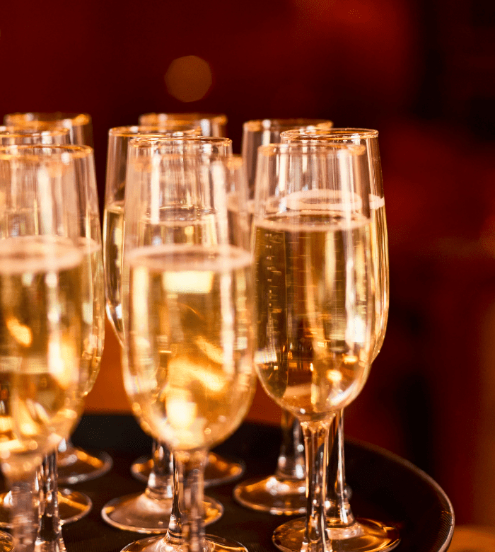 A close-up of several champagne glasses filled with sparkling wine, arranged on a black serving tray with a warm, blurred background.