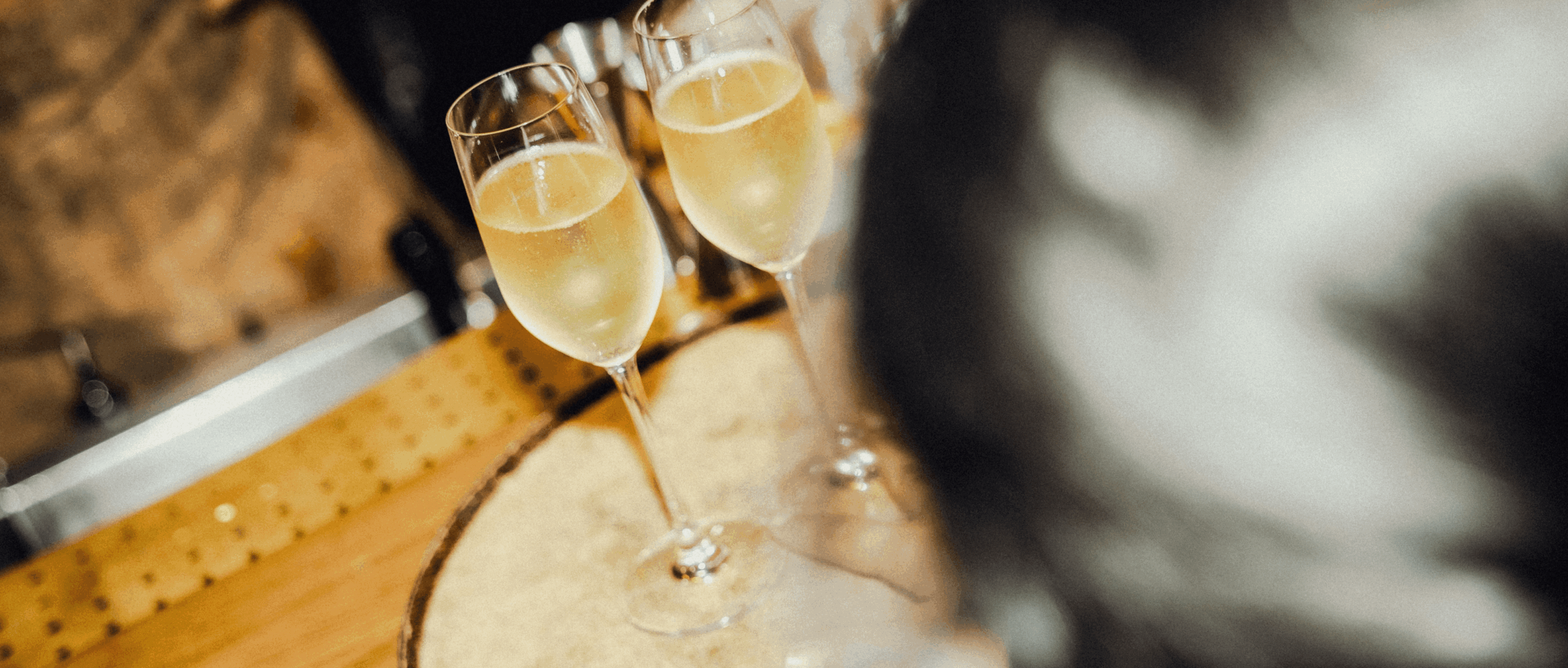 Two glasses of champagne on a wooden surface, with a blurred foreground and background, creating a warm and festive atmosphere.