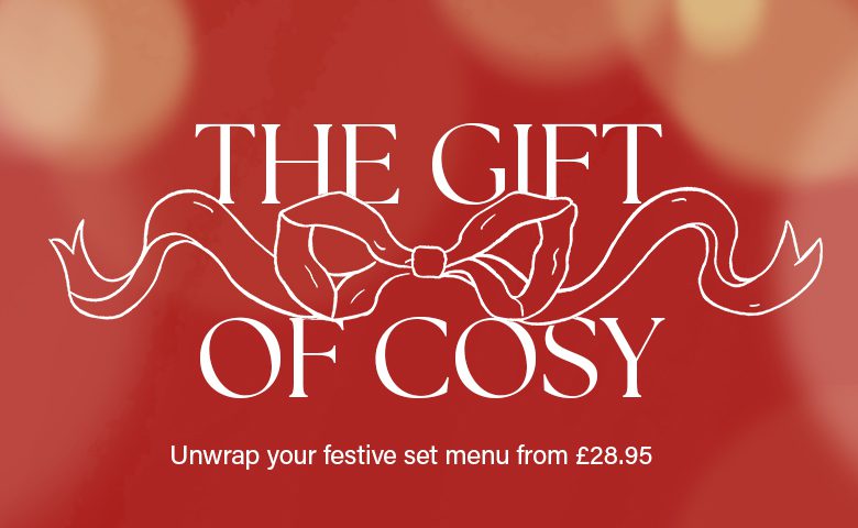 Red background with blurred lights, white text reads "The Gift of Cosy" with a ribbon illustration. Smaller text below says, "Unwrap your festive set menu from £28.95.